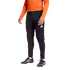 A person wearing an orange long-sleeved top, black Adidas goalkeeper pants with padded knees, and black soccer cleats against a dark background.