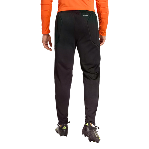 Rear view of a person wearing black Climacool athletic pants and soccer cleats, wearing an orange long-sleeved top against a black background.