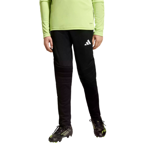 Person wearing a lime green long-sleeve shirt, black padded soccer pants, and black cleats against a black background.