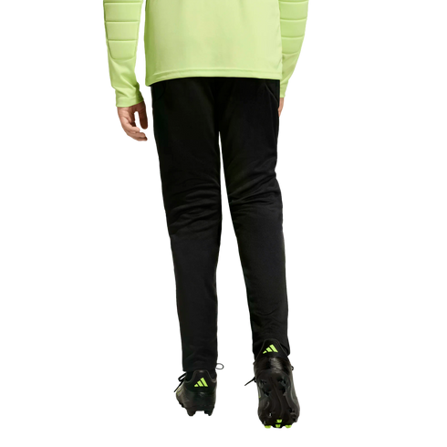 Back view of a person wearing a neon yellow long-sleeved jersey, black training pants, and black soccer cleats with neon accents against a black background.