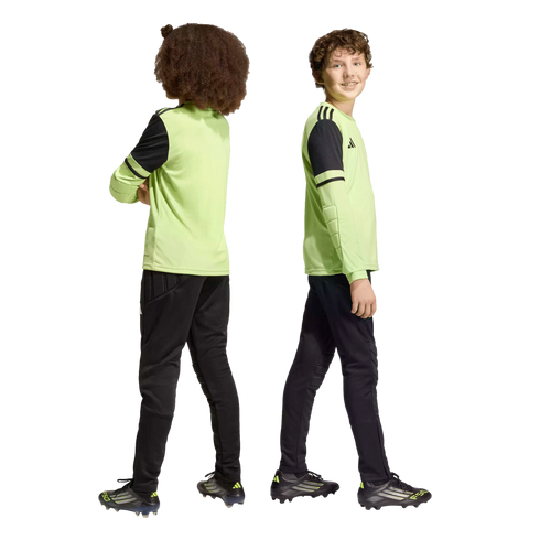 Two boys in lime green and black soccer uniforms standing back-to-back against a black background.