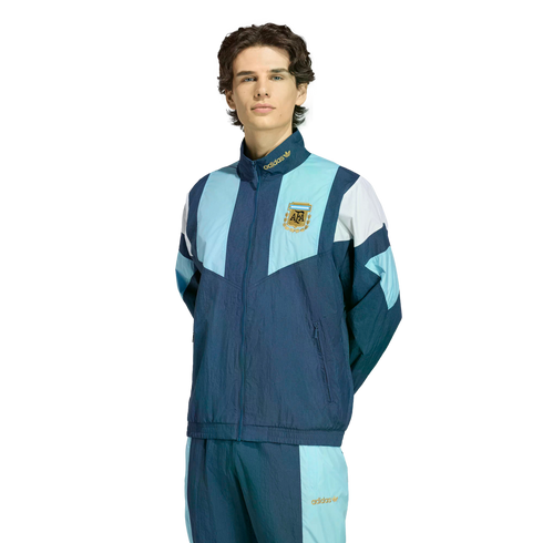 Man wearing a navy and light blue Adidas tracksuit with the Argentina Football Association logo on the chest, standing against a white background.