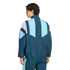 Rear view of a man wearing a blue and white geometric color-blocked windbreaker and matching track pants against a plain white background.