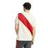 Rear view of a man wearing a cream t-shirt with a bold red diagonal stripe and dark shorts with red stripes, standing against a plain white background.