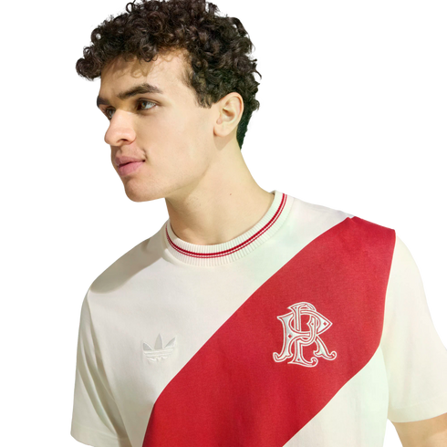 A young man with curly hair wearing a white Adidas t-shirt with a bold red diagonal sash across the chest.