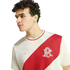 A young man with curly hair wearing a white Adidas t-shirt with a bold red diagonal sash across the chest.