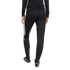 Rear view of a person wearing black Adidas track pants with white stripes on the side, a matching long-sleeved top, and soccer cleats against a light gray background.