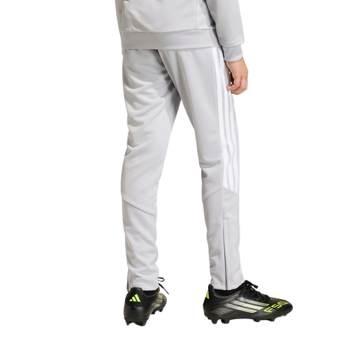 Rear view of a person wearing light gray track pants with white side stripes and black soccer cleats with neon green accents.