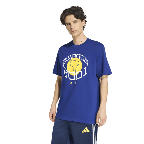 A male model in a blue Adidas t-shirt with a yellow South America graphic and "25 ANOS 2001" text, paired with matching blue athletic shorts.