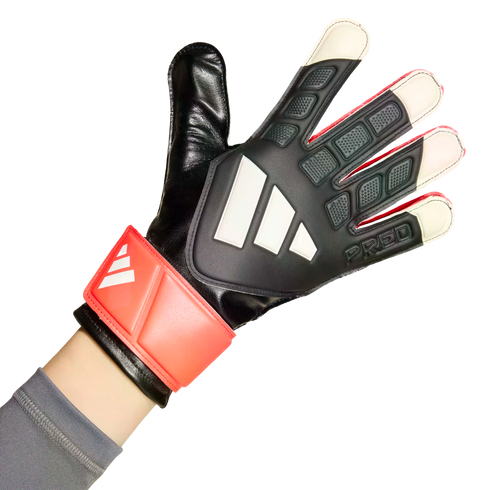 Close-up of a hand wearing a black Adidas Predator goalkeeper glove with three white stripes and a red wrist strap, set against a white background.