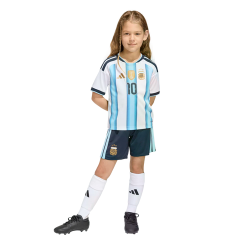 A young girl with braided hair posing in a full Argentina national football team kit, including a #10 jersey, navy shorts, white socks, and black cleats.