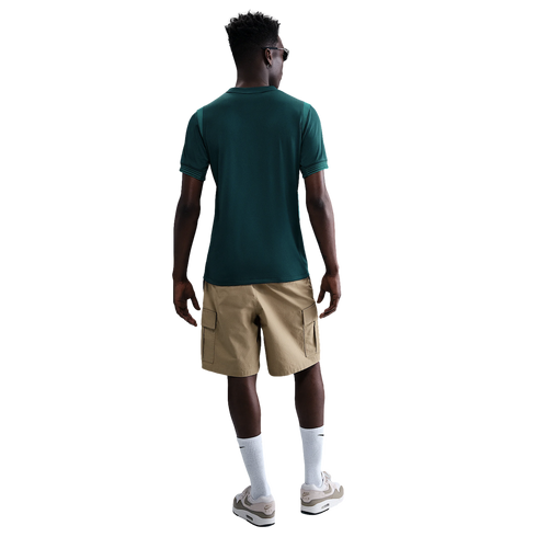 Back view of a man wearing a dark green t-shirt, tan cargo shorts, white crew socks, and beige sneakers against a white background.