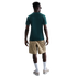 Back view of a man wearing a dark green t-shirt, tan cargo shorts, white crew socks, and beige sneakers against a white background.