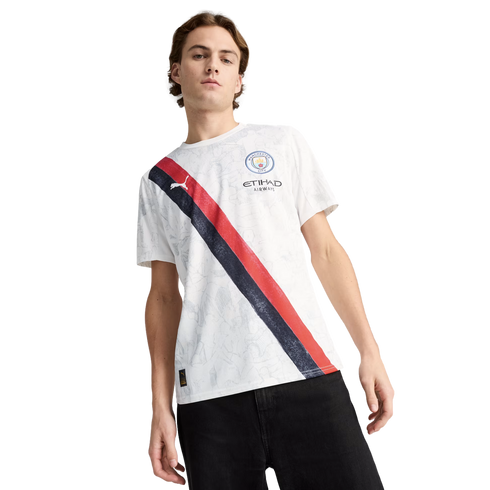 A man wearing a white Manchester City jersey with a navy and red diagonal stripe and black pants, standing against a white background.