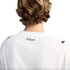 A rear view of a person with wavy brown hair wearing a white t-shirt featuring a cursive "KidSuper" logo on the upper back and Puma logos on the shoulders.