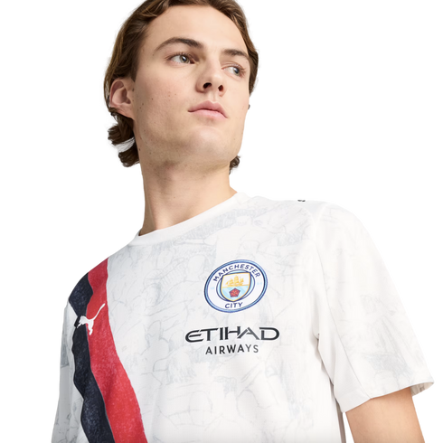 A young man looking to the side while wearing a white Manchester City jersey featuring a red and blue diagonal sash.