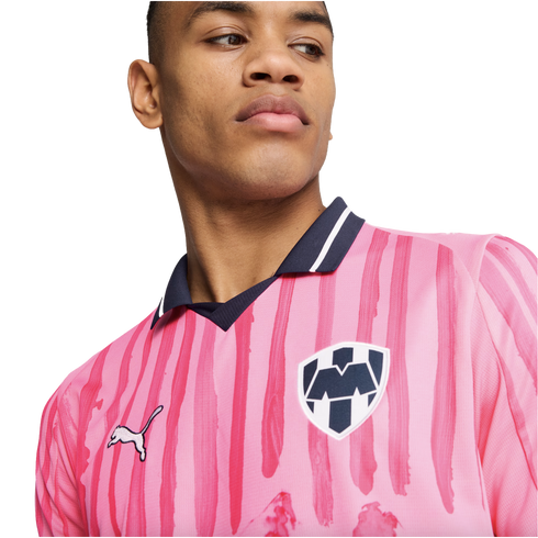 A man wearing a pink C.F. Monterrey soccer jersey with dark pink stripes, a navy collar, and the team crest, looking to the side against a white background.