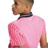 Side profile of a person wearing a pink Puma jersey with red striped sleeves and a navy blue collar. The jersey features a white Puma logo and "KidSuper" text on the back.