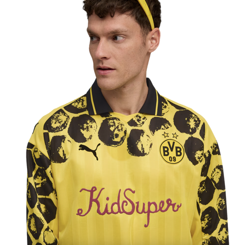 A man wearing a yellow and black KidSuper x Puma BVB long-sleeve jersey with a spotted pattern on the sleeves and shoulders against a white background.