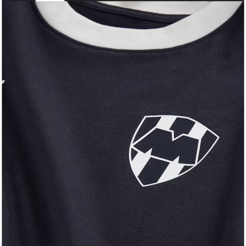 Close-up of a navy blue jersey with a white collar. On the chest is the C.F. Monterrey shield crest, featuring a stylized 'M' over vertical black and white stripes.