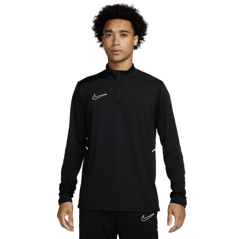 A young man with curly hair and freckles wearing a black Nike quarter-zip long-sleeve athletic top and matching black pants, standing against a white background.