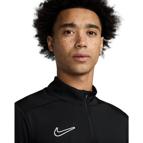 A close-up portrait of a young man with curly hair and freckles wearing a black Nike quarter-zip athletic top against a white background.