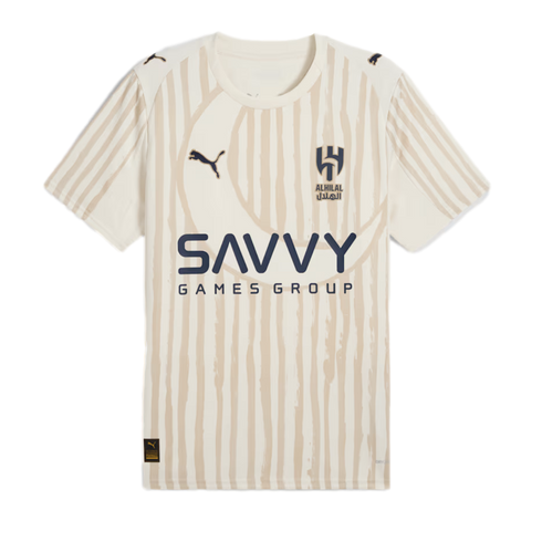 An Al Hilal football jersey in cream with beige vertical stripes and a subtle crescent moon. Features Puma logos, the club crest, and "SAVVY GAMES GROUP" printed across the center.