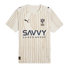 An Al Hilal football jersey in cream with beige vertical stripes and a subtle crescent moon. Features Puma logos, the club crest, and "SAVVY GAMES GROUP" printed across the center.