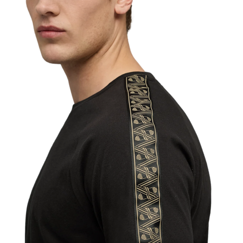 Side profile of a person wearing a black t-shirt with a tan patterned stripe along the shoulder and sleeve, against a solid black background.