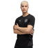 A man with blonde hair wears a black Puma Manchester City training shirt. He stands with arms crossed against a black background, holding a water bottle.