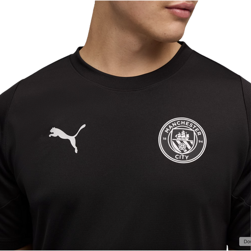 A person wearing a black Manchester City football shirt with a white Puma logo and the club's monochrome crest on the chest.