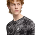 Man with red curly hair wearing a grey and black patterned Manchester City Puma jersey, looking off-camera against a black background.