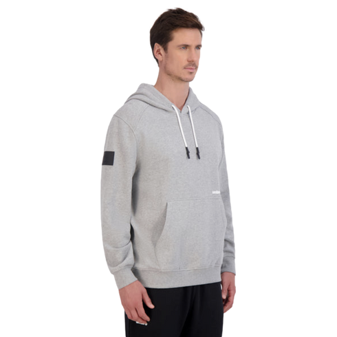 Man wearing a grey hoodie with white drawstrings and black sweatpants, standing against a plain black background.