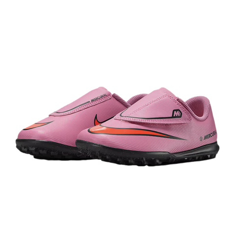 A pair of pink Nike Mercurial kids' soccer shoes with orange swooshes and black studded soles, featuring velcro strap closures, shown against a black background.