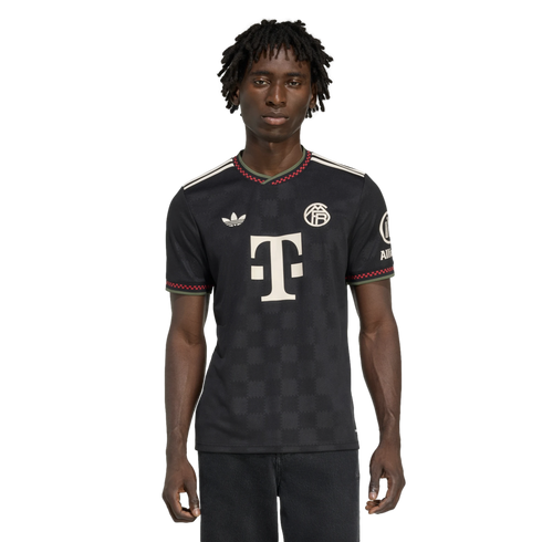 Man wearing a black Bayern Munich soccer jersey with white logos and red and green trim on the collar and sleeves, against a black background.