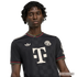 A Black man with dreadlocks wears a black FC Bayern Munich football jersey featuring a large white "T" logo and red checkered trim.