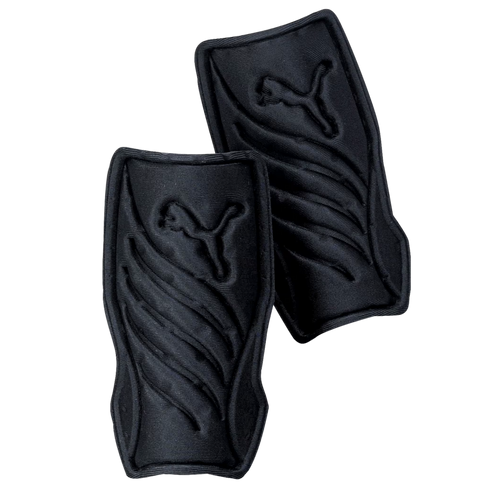 A pair of black Puma soccer shin guards with embossed leaping cat logos and curved ridges, set against a black background.
