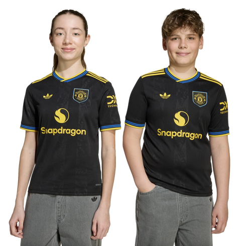 Two young people wearing matching black Manchester United jerseys with yellow "Snapdragon" logos, standing against a plain black background.