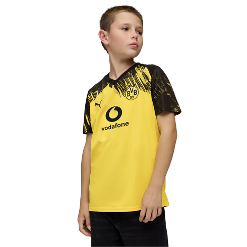 A boy wearing a yellow and black Borussia Dortmund soccer jersey with the BVB and Vodafone logos, looking to the side against a black background.