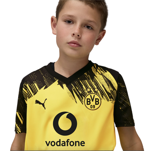 A young boy wearing a yellow and black Borussia Dortmund Puma soccer jersey with a Vodafone sponsor logo against a black background.