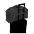 A black duffel bag with a trolley sleeve secured over the telescopic handle of a suitcase, against a black background.