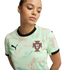 Young woman wearing a mint-green Puma Portugal soccer jersey with black trim and a red and green dotted pattern, looking down against a black background.