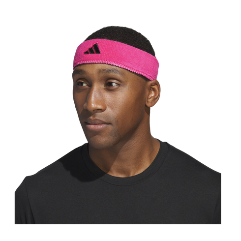 Close-up of a man wearing a bright pink Adidas headband and a black t-shirt against a black background.