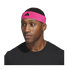 Close-up of a man wearing a bright pink Adidas headband and a black t-shirt against a black background.