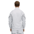 Back view of a person in a white track jacket with black sleeve piping and matching pants, standing against a solid black background.