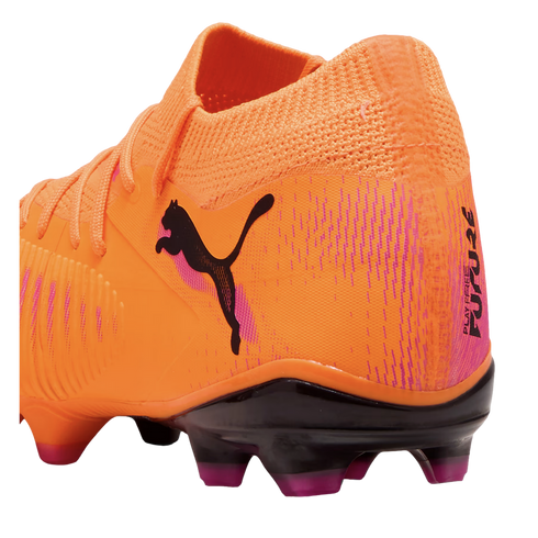 Bright orange Puma soccer cleat with a black cat logo, pink accents, and black studs with purple tips. The heel features the text "PLAY FREE FUTURE."