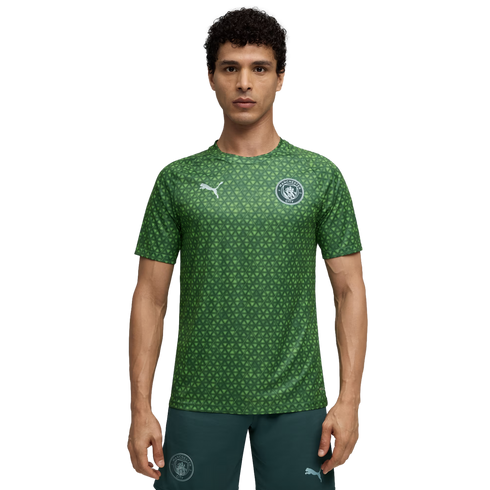 A man wearing a green, patterned Manchester City training jersey and dark green shorts.