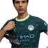 Man wearing a teal patterned Manchester City jersey holds a black Puma soccer cleat over his shoulder against a black background.