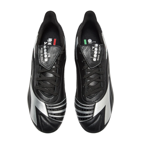 Overhead view of black and silver Diadora soccer cleats with fold-over tongues against a black background.