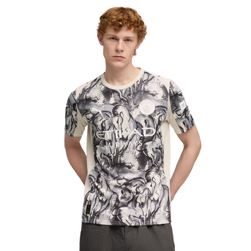 Man with curly red hair wearing a white and black marble-patterned soccer jersey with the Etihad Airways logo, posed against a solid black background.